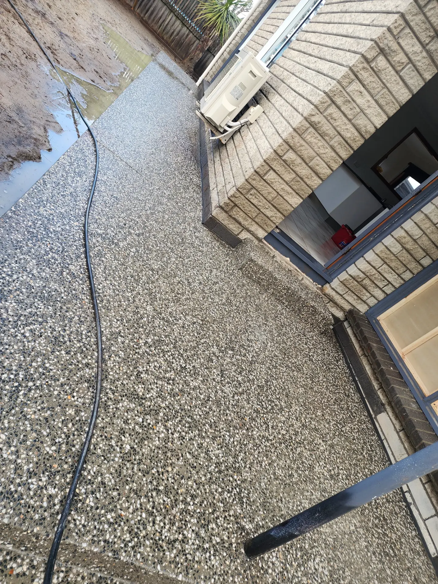 An exposed aggregate path wrapping the corner of a brick house with washed stone flush in the surface